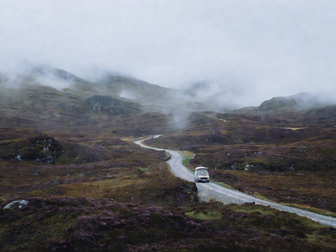 Campervan on an empty single-track road through a highland valley under low cloud